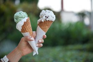 Two colorful tasty ice cream cones in hand.